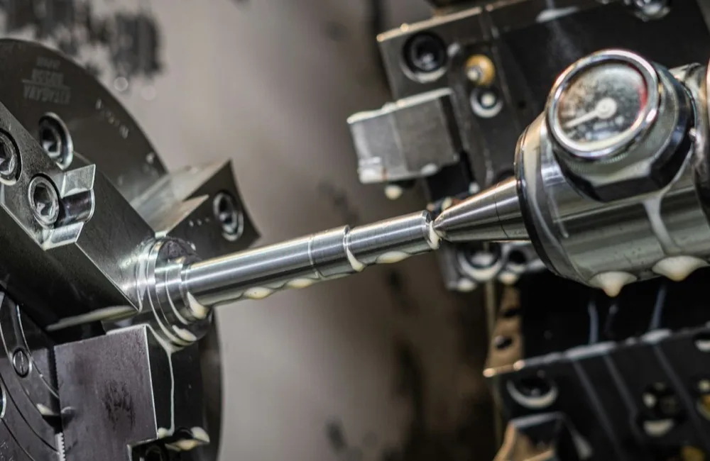A CNC lathe turning a metal shaft, held in a three-jaw chuck with a live center