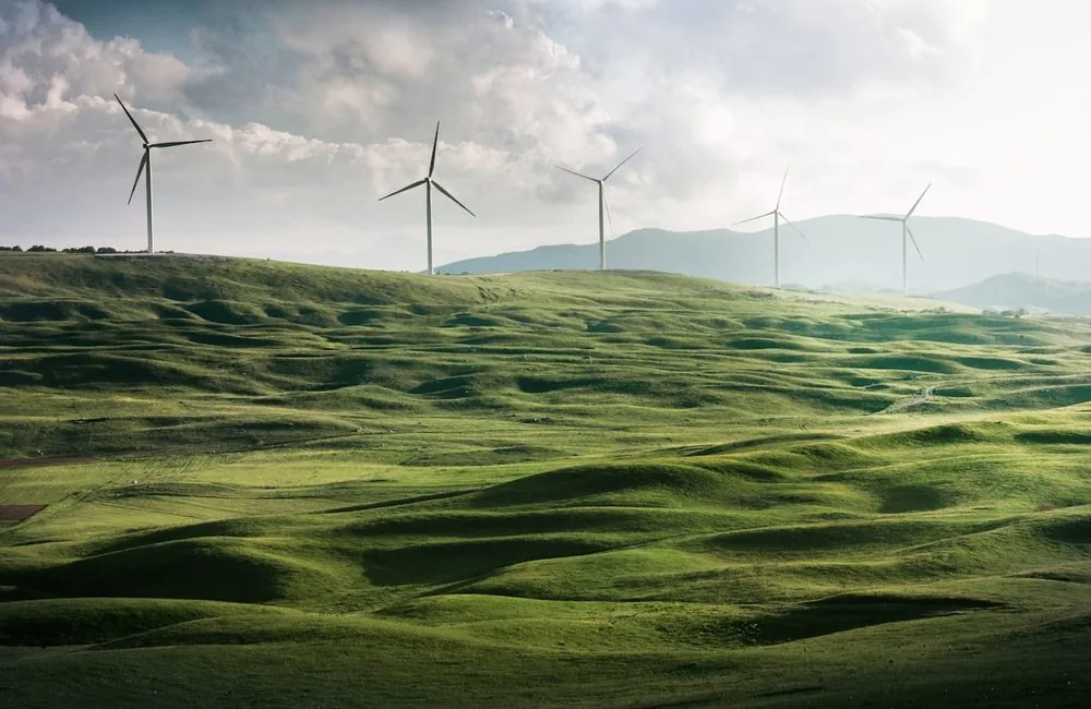 A line of wind turbines along a ridge of green rolling hills under a bright sky