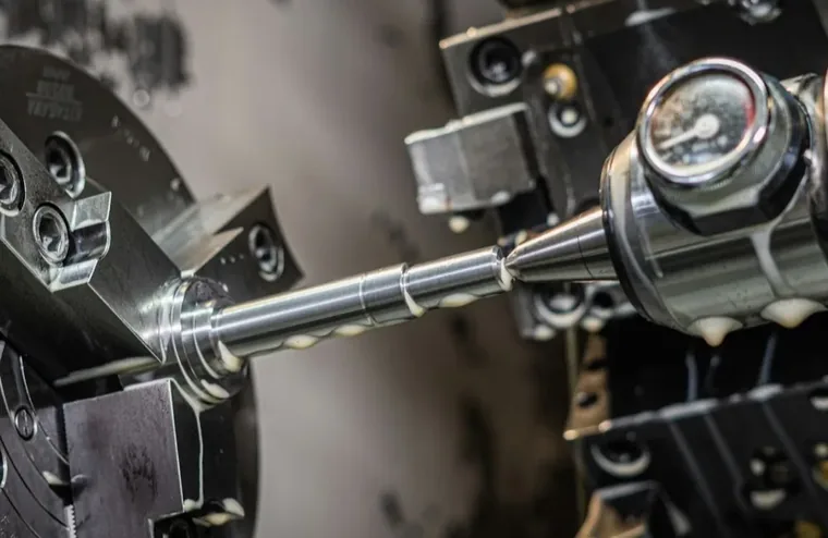 A CNC lathe turning a metal shaft, held in a three-jaw chuck with a live center