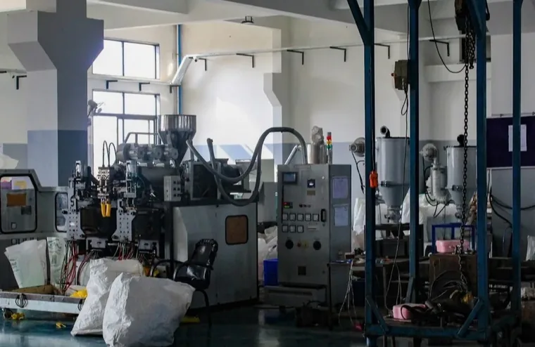 A plastics moulding machine on a factory floor, with hoppers and a control panel