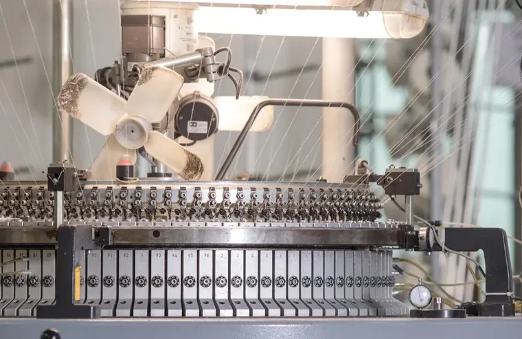 A knitting machine with rows of needles and threads feeding in